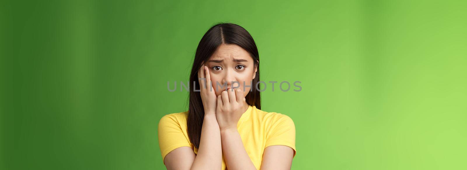 Innocent insecure timid asian scared girl panicking, standing afraid victim terrified, touch cheek shocked, frowning stunned, biting fingernails, anxiously stare camera, green background by Benzoix