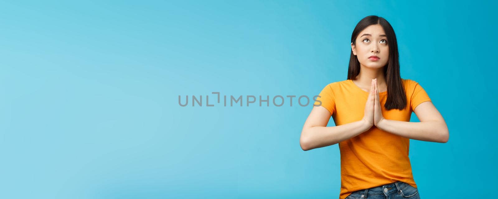 Serious-looking hopeful cute asian woman begging god hear prayers, supplicating, making wish look up sky talking lors, believe have faith, stand blue background pleading good fortune luck by Benzoix