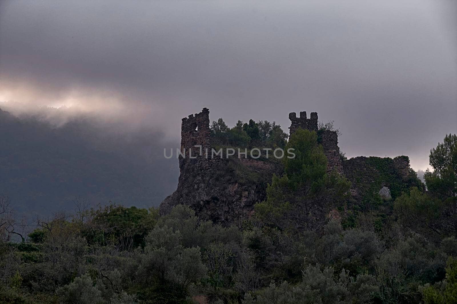 Jinquer, Castellon, Spain. Ruins of abandoned castle on top of mountain.Mediterranean forest, olive trees, pines, sky with storm clouds
