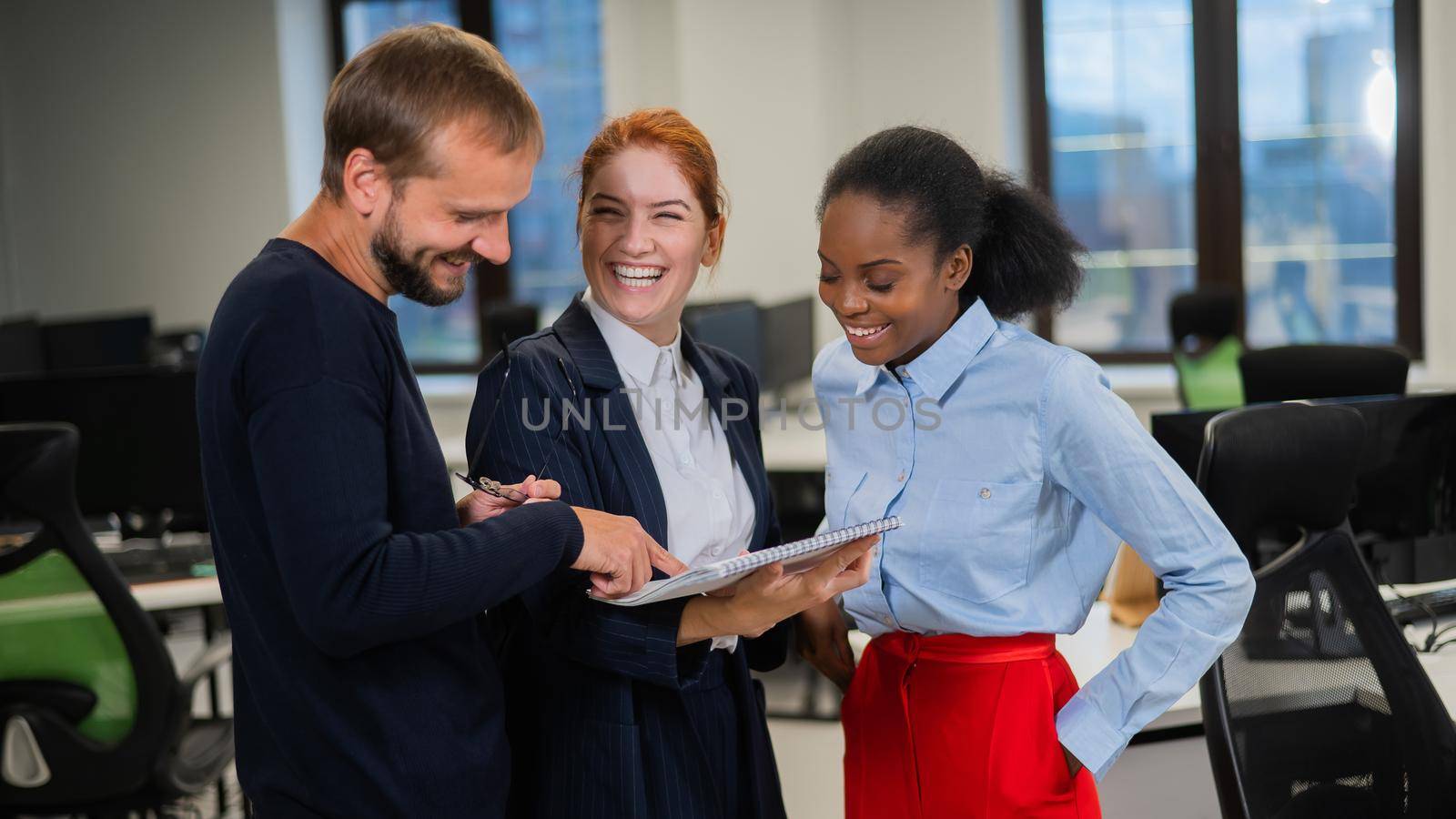 Colleagues discuss work. African young woman, caucasian man and red-haired caucasian woman communicate in the office