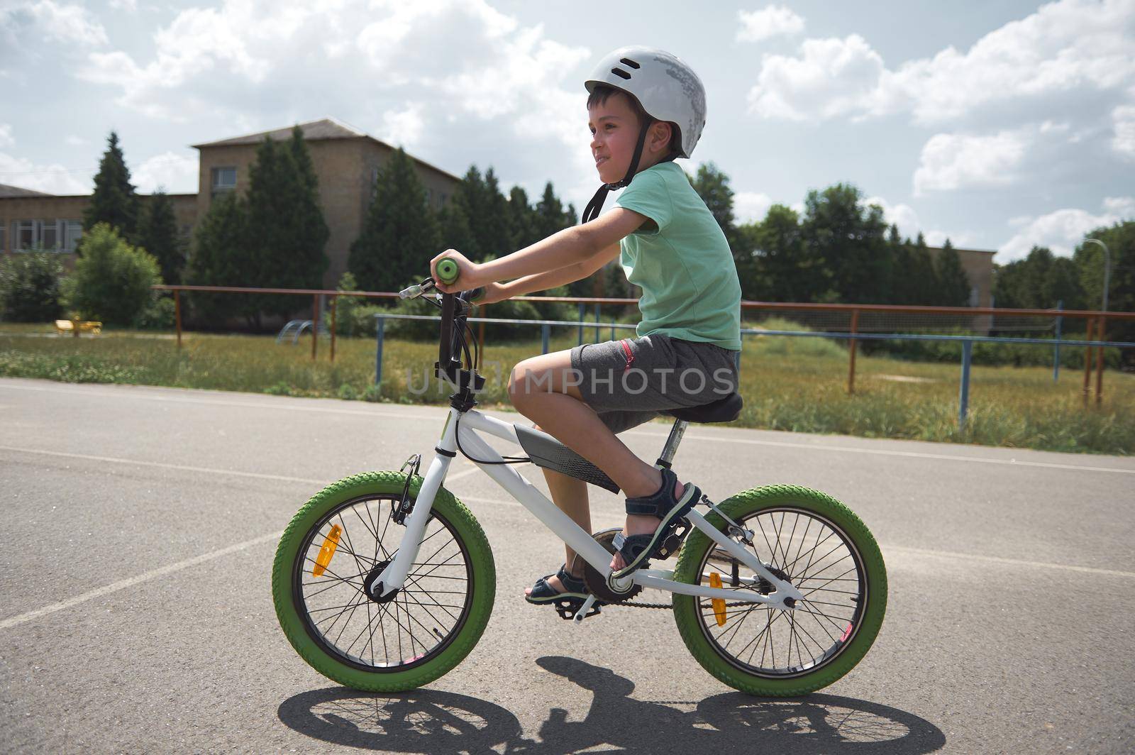Active sporty Caucasian schoolboy, wearing sports helmet cycling on a bicycle on the asphalt road in urban environment. Active lifestyle and sport concept