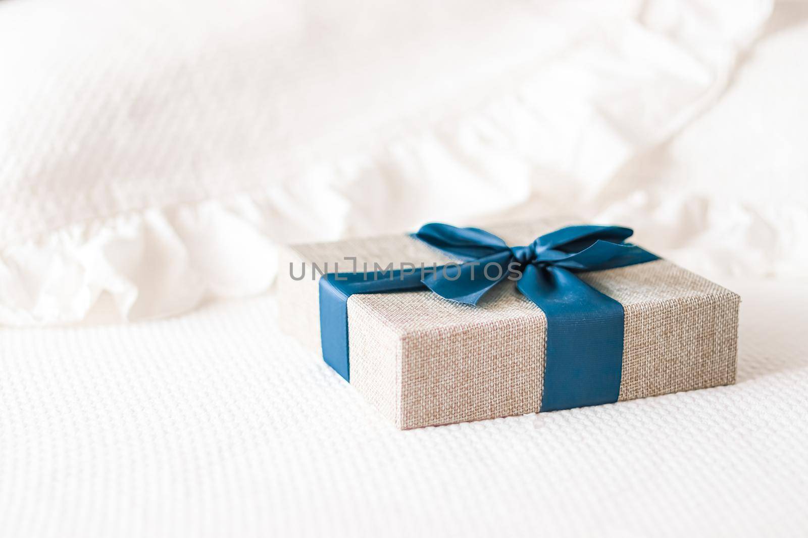 Holiday present and luxury online shopping delivery, wrapped linen gift box with blue ribbon on bed in bedroom, chic countryside style, close-up