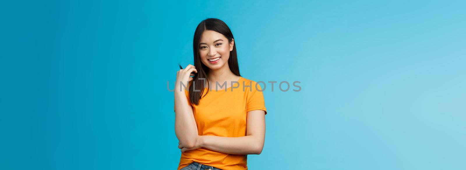 Cheerful asian girl with dark short haircut touching hair strand smiling lively, cross one arm chest, laughing, carefree talking casually friends, discuss university lifestyle, blue background by Benzoix