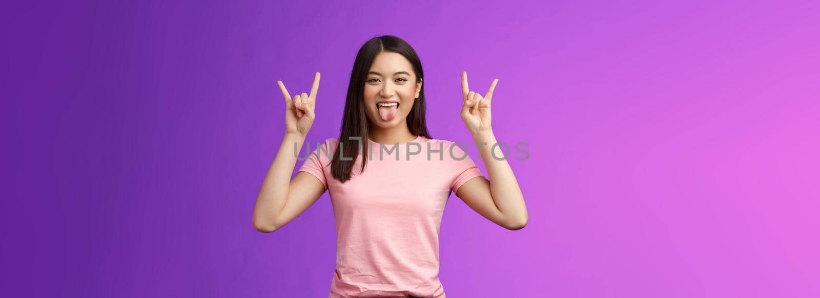 Rebellious amused asian girl enjoy rock-n-roll, attend awesome concert have fun, show tongue make heavy-metal gesture, express excitement and joy, stand purple background cheerful by Benzoix
