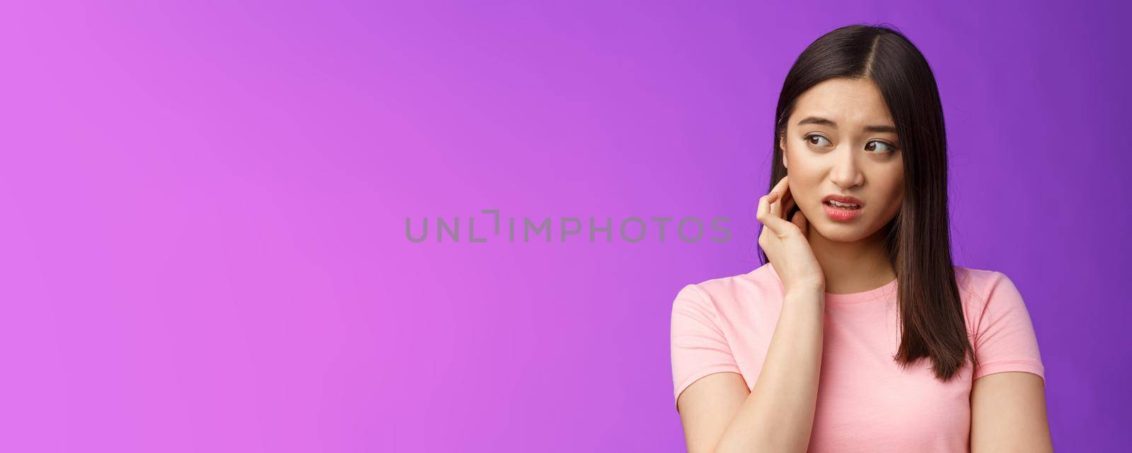 Insecure anxious young timid asian girl feel nervous scared, scratch neck worried, look sideways alarmed, feel danger, standing upset purple background distressed suffer discomfort by Benzoix