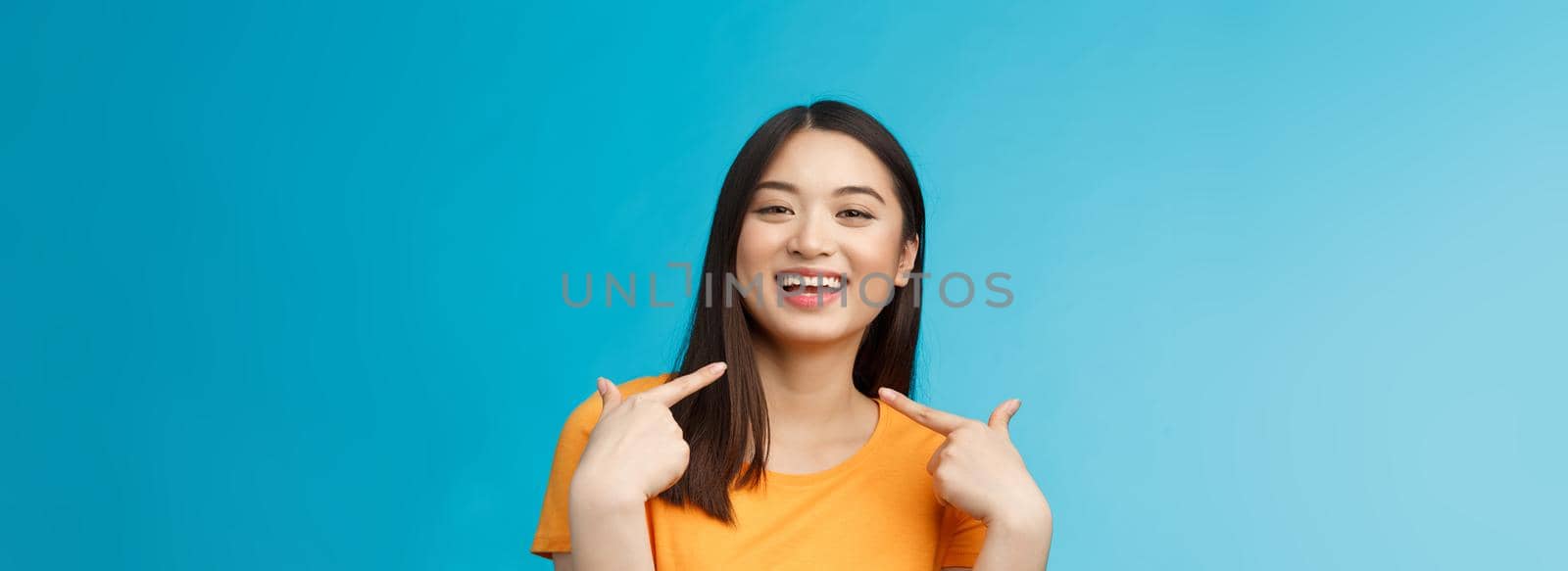 Close-up proud boastful cute asian girl telling story pointing herself, smiling broadly, bragging new haircut, standing pleased, delighted tell big news, stand blue background upbeat.