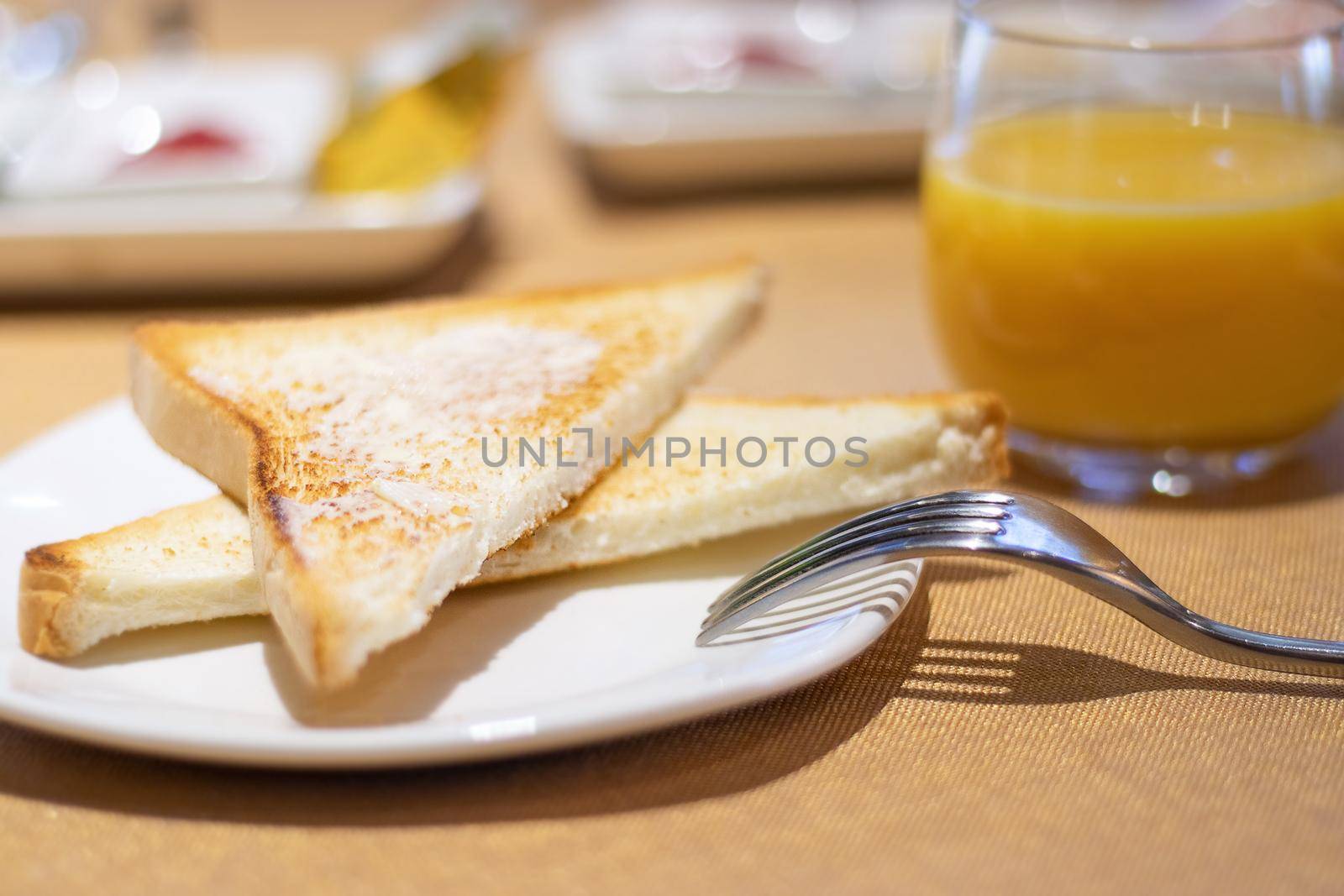 breakfast toasted toast with butter on a white plate and orange juice. soft focus