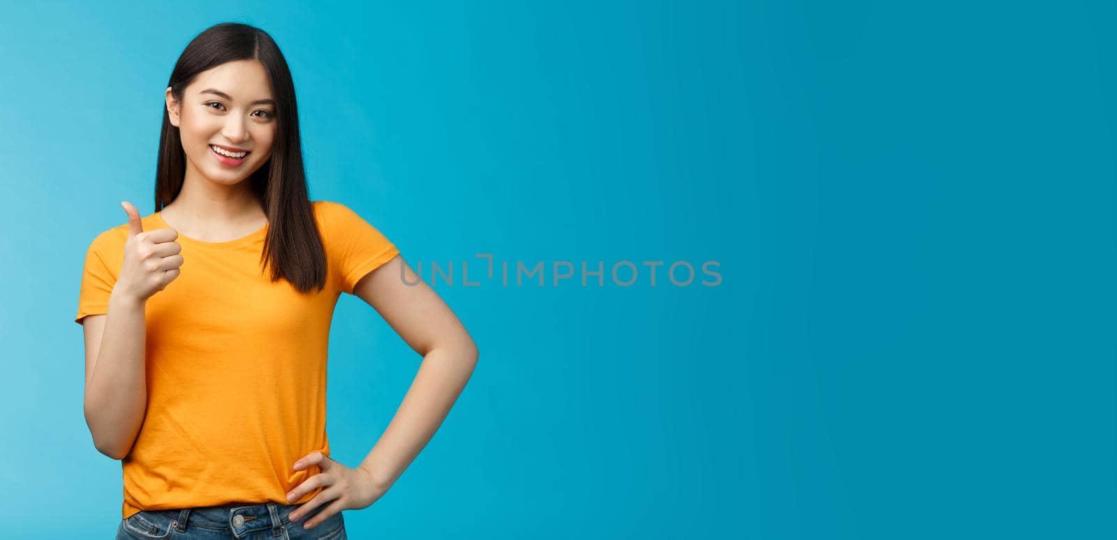 Confident cheerful asian brunette girl show thumb-up satisfied, give approval, liking good choice, smiling delighted, accept your plan, positive judgement, stand blue background by Benzoix