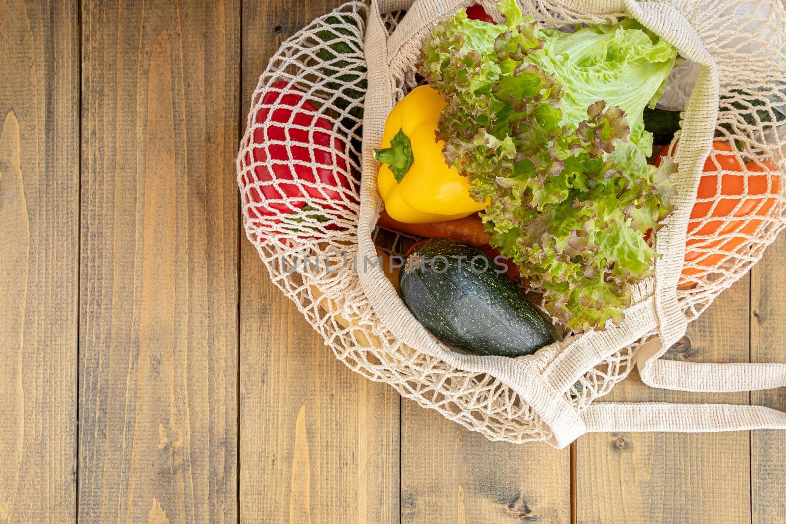 top view of bell peppers, zucchini and lettuce in a reusable bag. fresh vegetables in eco bag on wooden background. eco concept and respect for nature by Leoschka