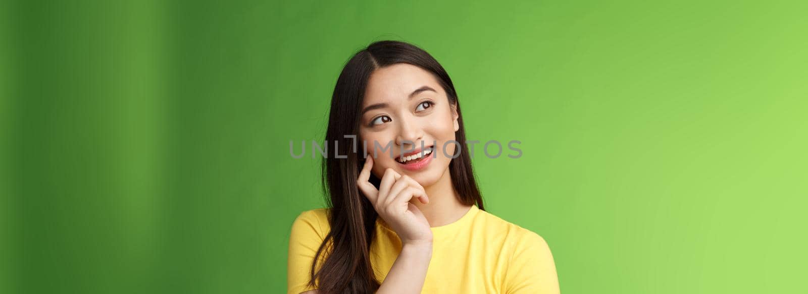 Close-up dreamy intrigued creative asian brunette woman imaging summer vacation trip, picturing perfect holiday, standing thoughtful, touch cheek, thinking look up, stand green background by Benzoix