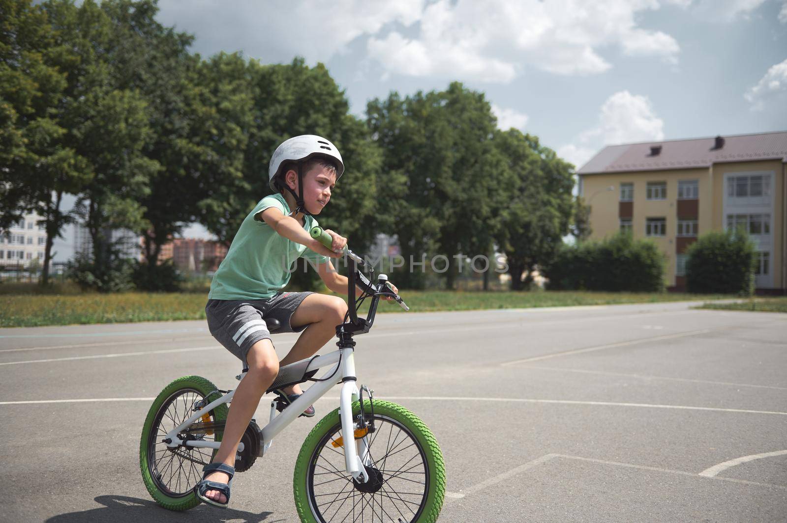Active sporty 10 years old European boy in sports helmet confidently riding bike. Caucasian school age child cycling on the city asphalt road. Healthy lifestyle. Physical exercises. Motion. Extreme