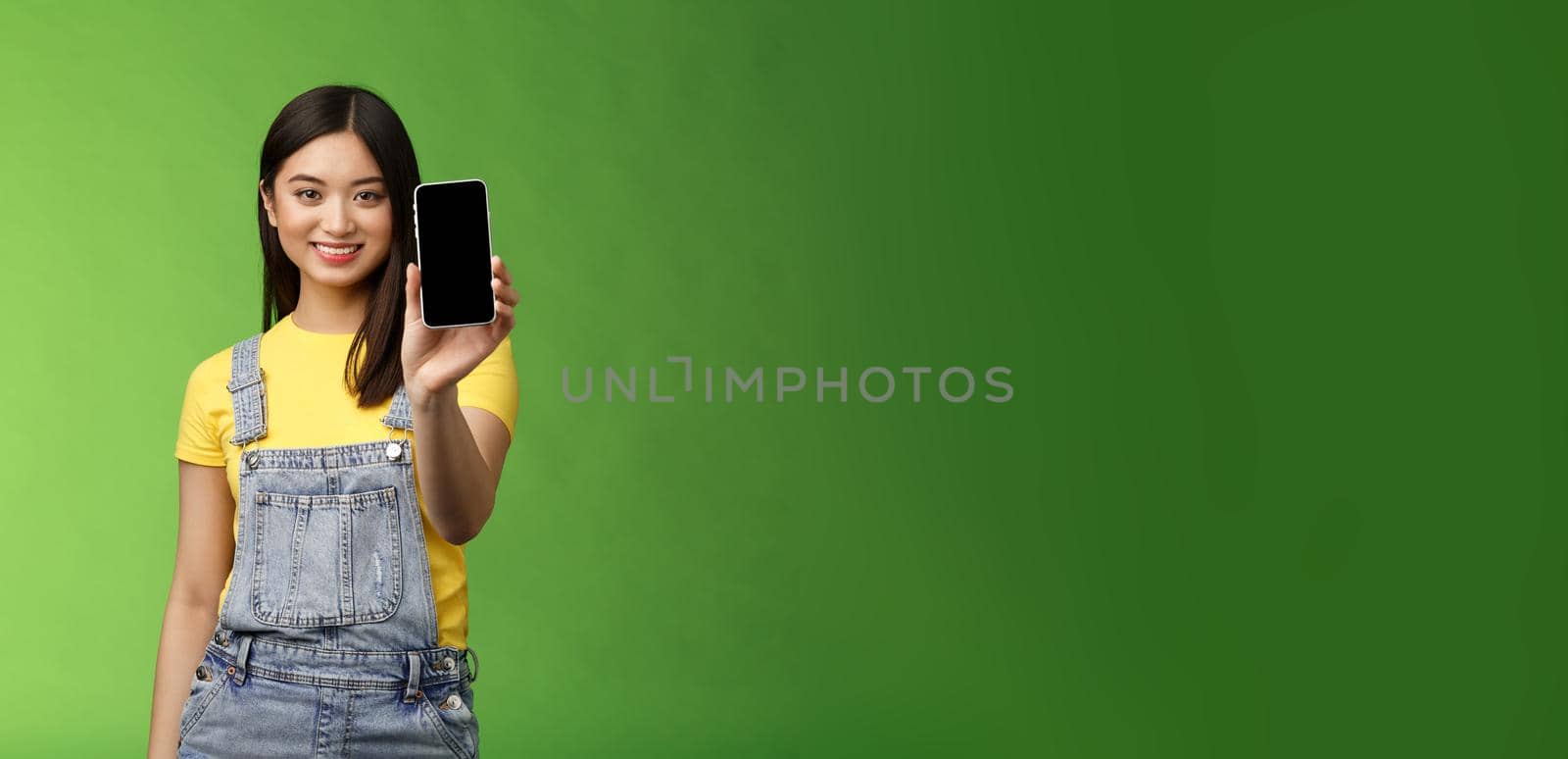 Confident assertive good-looking female asian introduce smartphone app, extend hand hold telephone arm, smiling delighted, recommend social profile, bragging own blog, green background by Benzoix