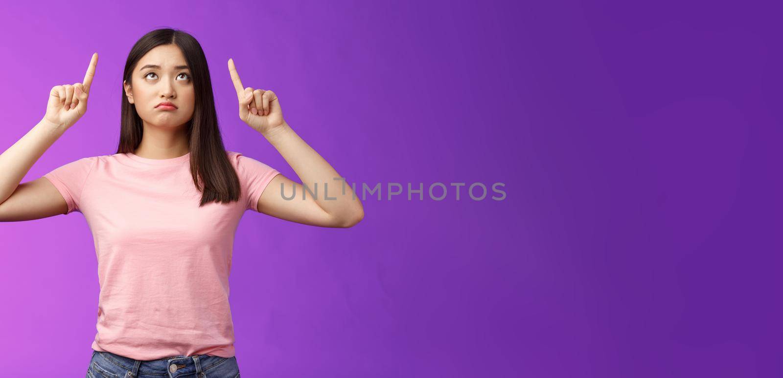 Sad disappointed sulking asian girl with short dark haircut, look pointing up upset, feel jealous, regret, missing good opportunity, staring unhappy top advertisement, stand purple background.