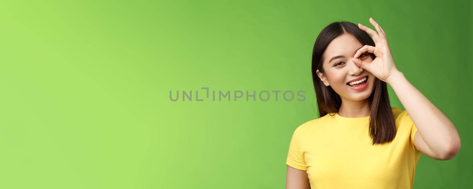 Close-up friendly carefree outgoing nice asian girl brunette having fun, tilt head joyfully, show okay ok sign look through circle amused, amazed perfect quality product, stand green background by Benzoix