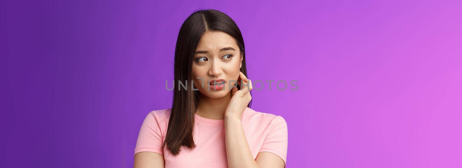 Insecure anxious young timid asian girl feel nervous scared, scratch neck worried, look sideways alarmed, feel danger, standing upset purple background distressed suffer discomfort.