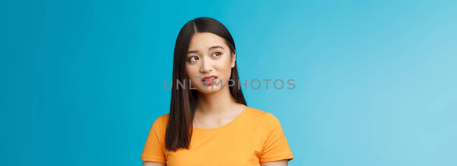 Doubtful unsure cute asian girl dark short haircut look left questioned, see strange thing, open mouth frowning upset uncertain, have hesitations, peek suspicious aside, stand blue background by Benzoix