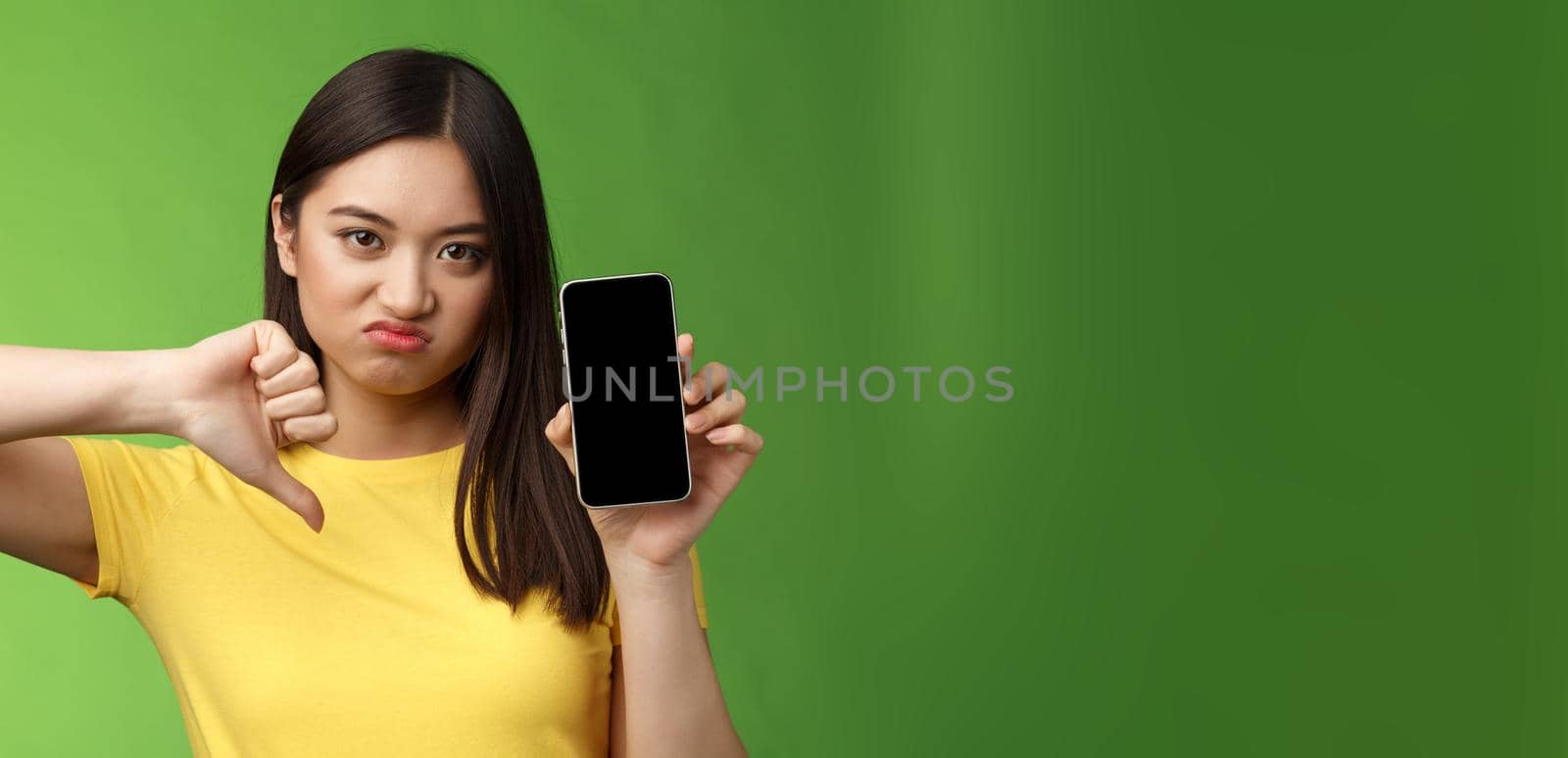 Close-up disappointed upset asian girl judging bad awful app, show smartphone screen, thumb-down grimacing displeased, give negative feedback, cannot stand ex-boyfriend new girlfriend by Benzoix