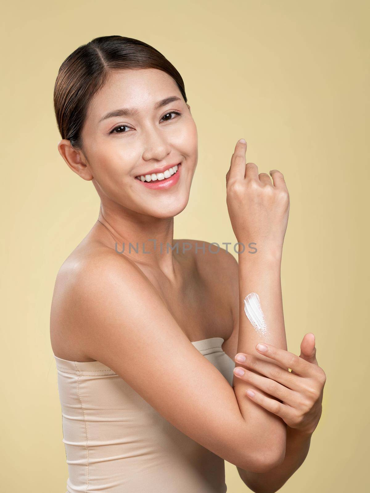 Ardent girl with soft makeup applying moisturizing skincare cream on her arm, isolated background. Skincare cream applied by female model concept.