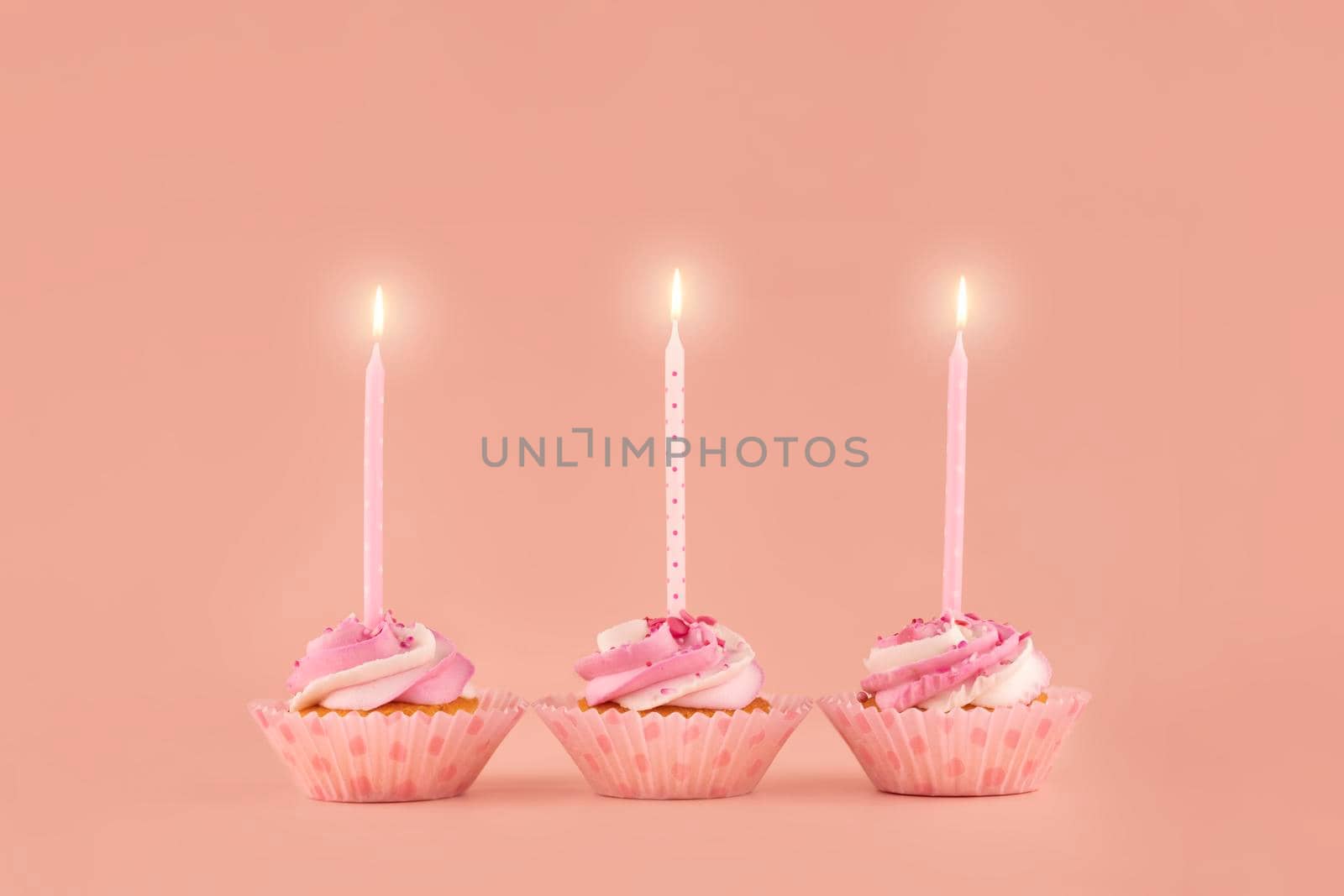 three birthday muffins cupcakes in pink wrappers with pink candles on a pink background high-quality photos for calendar and cards. Space for tex
