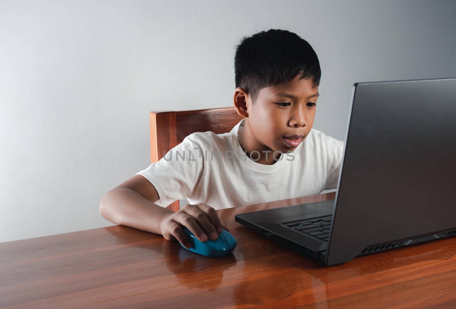 Close up The boy sits staring at the laptop and his hand is holding the mouse. educational concept, educational information search, copy space by Unimages2527