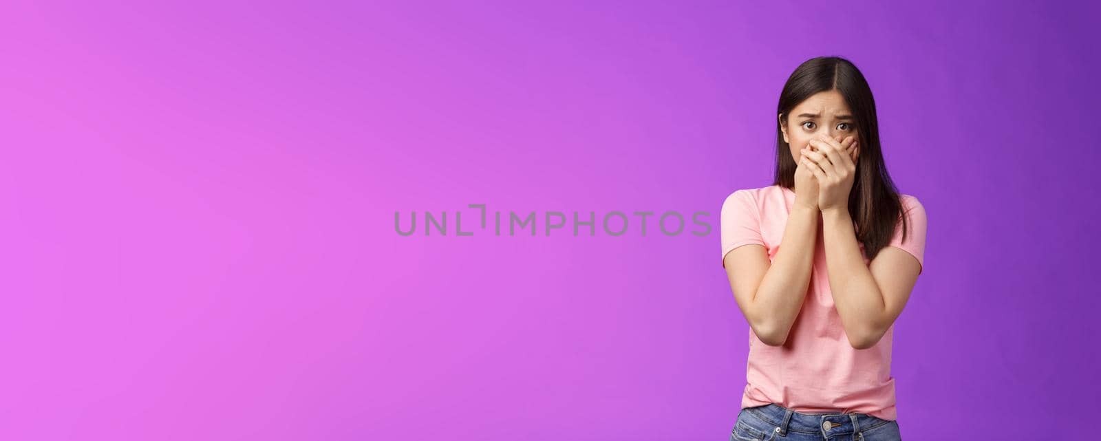 Shocked female asian victim frightened, gasping witness crime, close mouth hands, frowning, stare camera scared upset, make innocent terrified gaze, stand purple background. Copy space