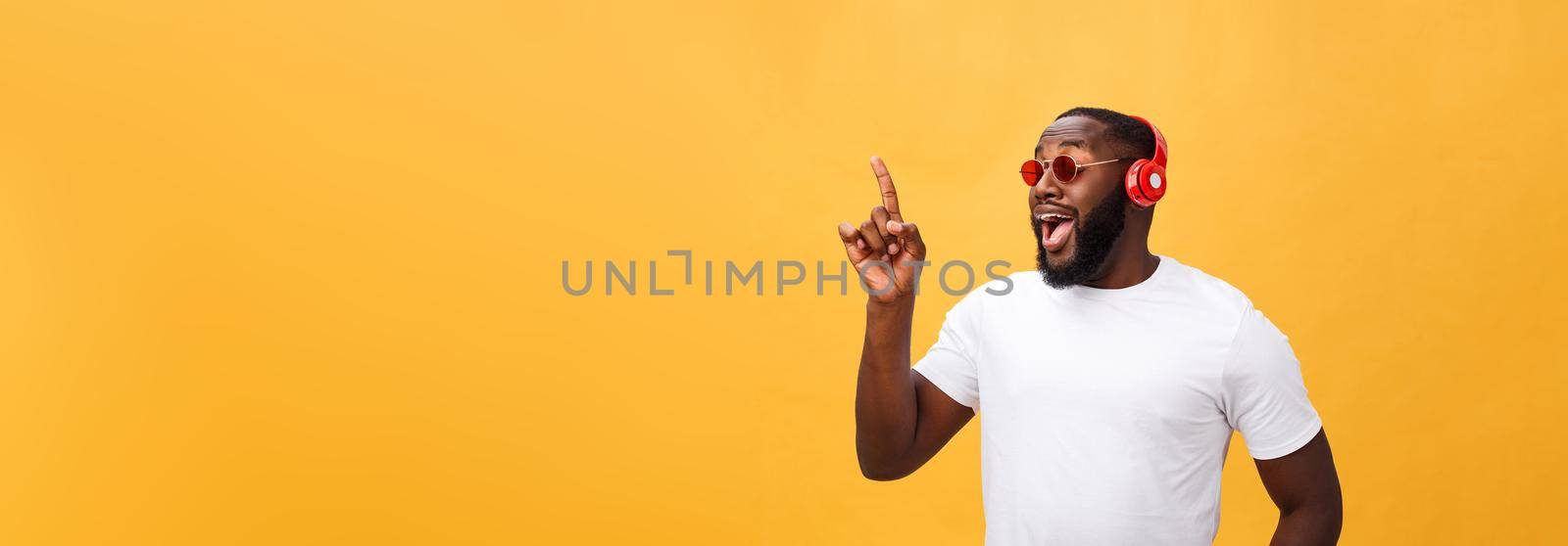 Handsome young African American man listening and smiling with music on his mobile device. Isolated over yellow background