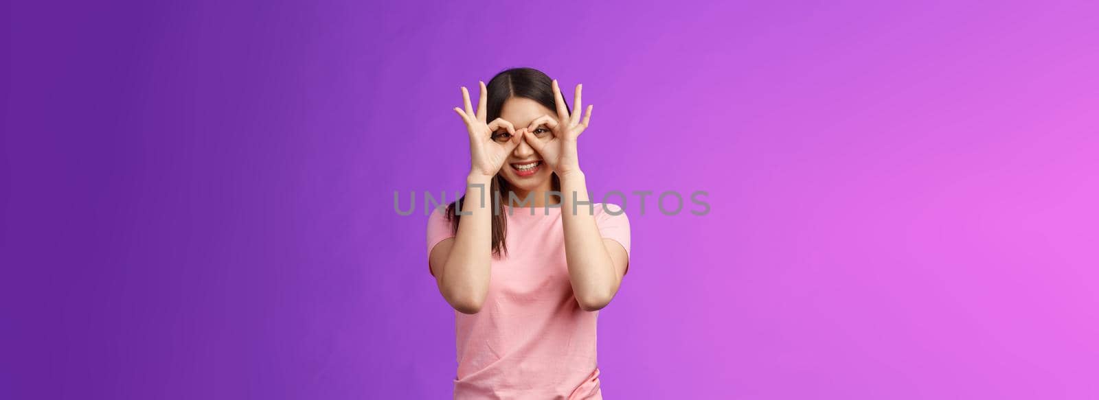 Cheerful friendly carefree asian woman having fun fool around, show okay ok signs on eyes make glasses from fingers, smiling delighted, mimicking funny emotions, stand purple background happy.