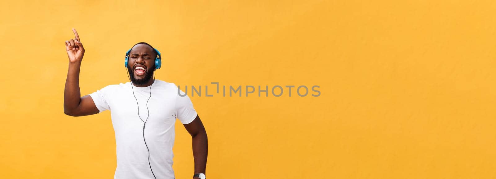 Young African American man wearing headphone and enjoy music dancing over yellow gold Background.