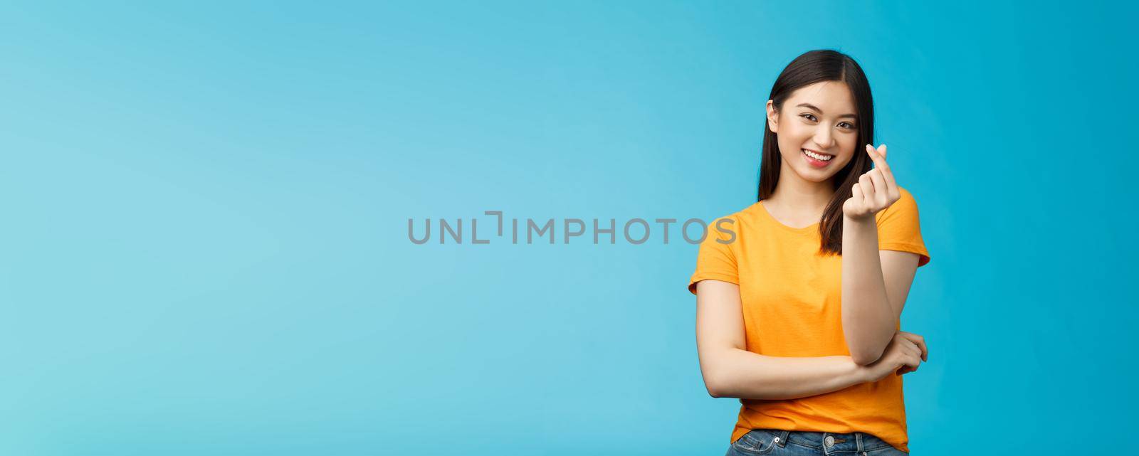Cheerful cute asian woman dark short haircut, show korean heart sign with fingers, smiling joyfully, express sympathy and caring feelings, confess love stand blue background, grinning upbeat by Benzoix