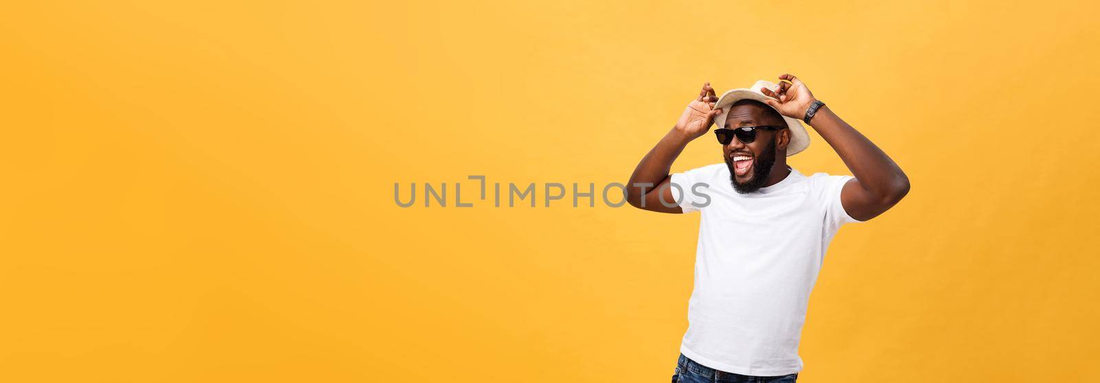 Close up portrait of a young man laughing with hands holding hat isolate over yellow background.