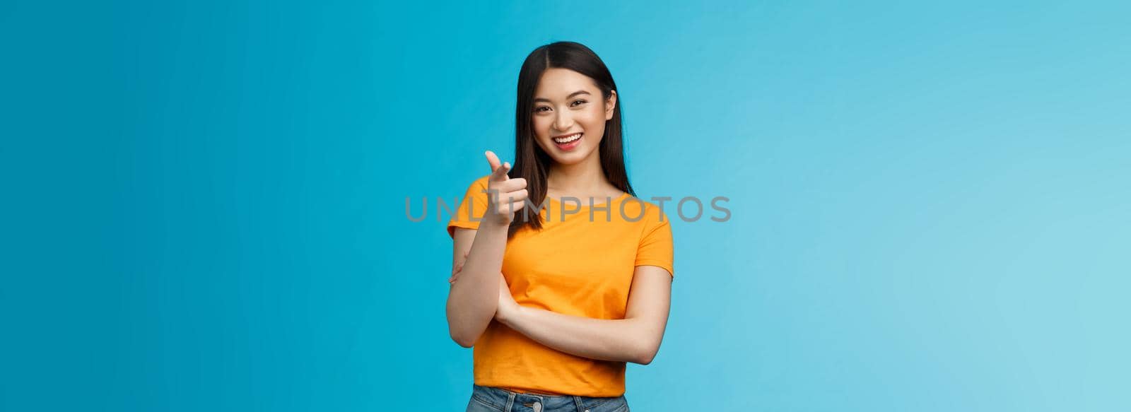 Hey you got point. Cheerful cute asian lively girl dark short haircut pointing camera finger-pistol smiling broadly, encourage friend make move, congratulate coworker good job, stand blue background.