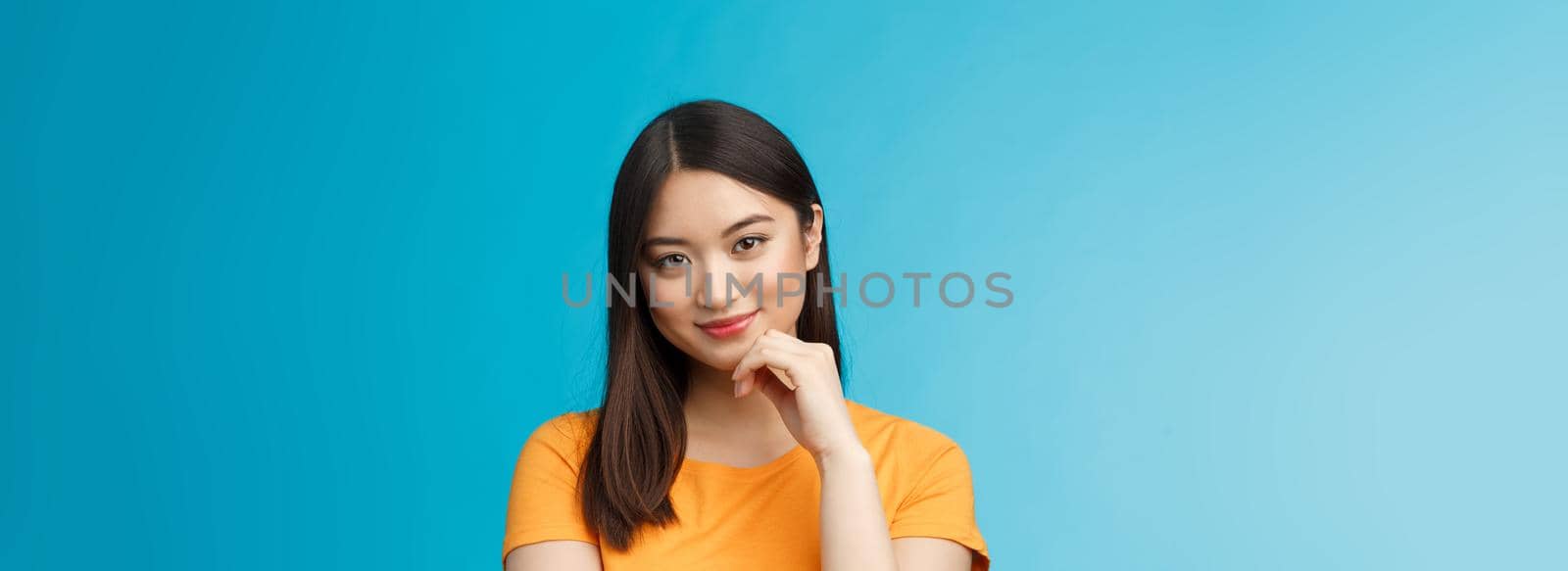 Close-up coquettish good-looking asian young modern woman curiously listen interesting story, smirking relaxed gaze camera, touch chin thoughtful, intrigued stand blue background.