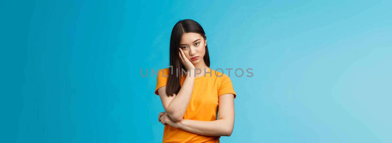 Sad bored asian female student attend boring uninteresting lecture lean face palm, look indifferent express apathy dislike, grimacing and sulking disappointed stand blue background bothered.