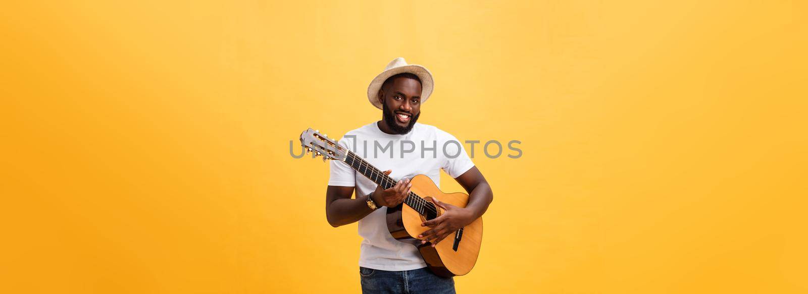 Muscular black man playing guitar, wearing jeans and white tank-top. Isolate over yellow background