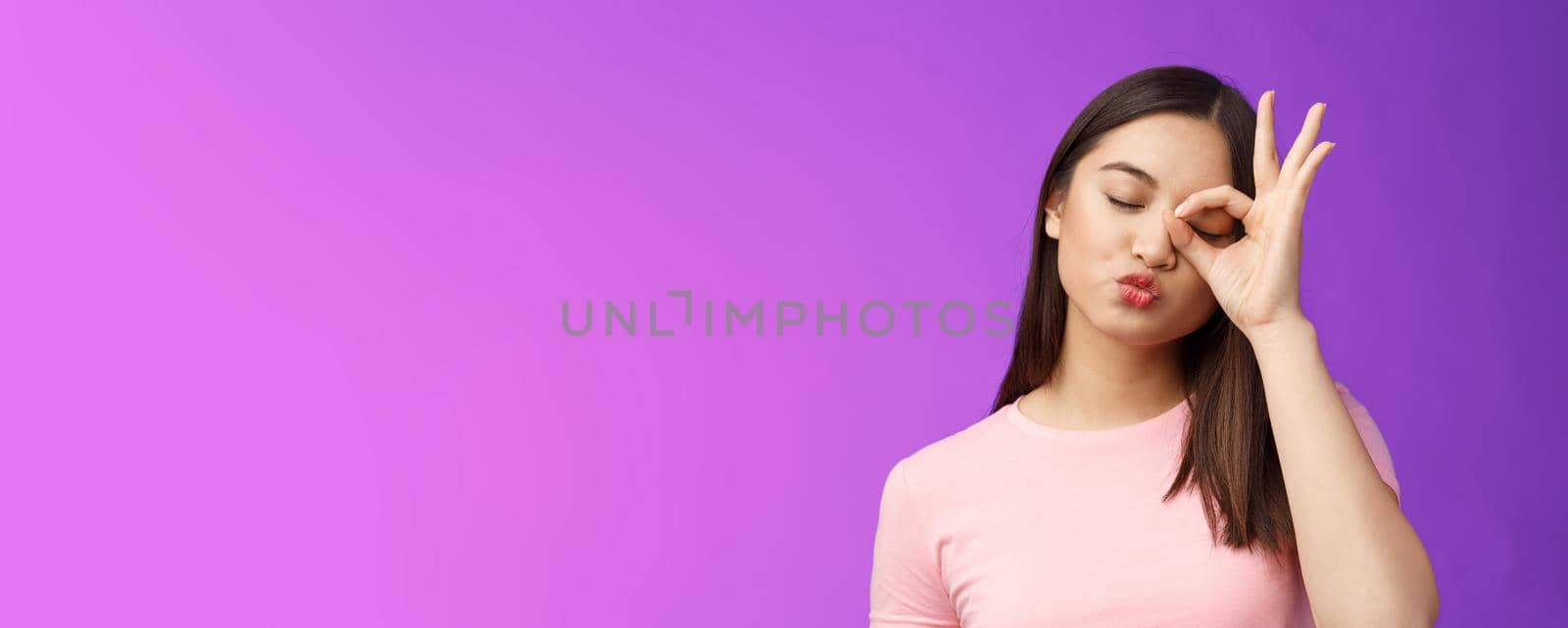 Cute silly asian female brunette folding lips kiss lovely expression, close eyes dreamy send muah, show perfection, okay ok sign, stand purple background carefree and cheerful. Copy space