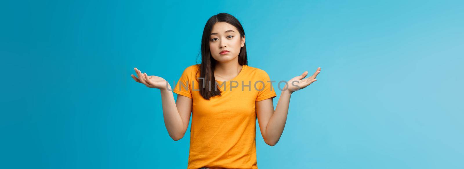 Shit happens. Indifferent absolutely careless female student not care how accident happened shrugging, look camera questioned unaware, hard answer, clueless how deal situation, stand blue background.