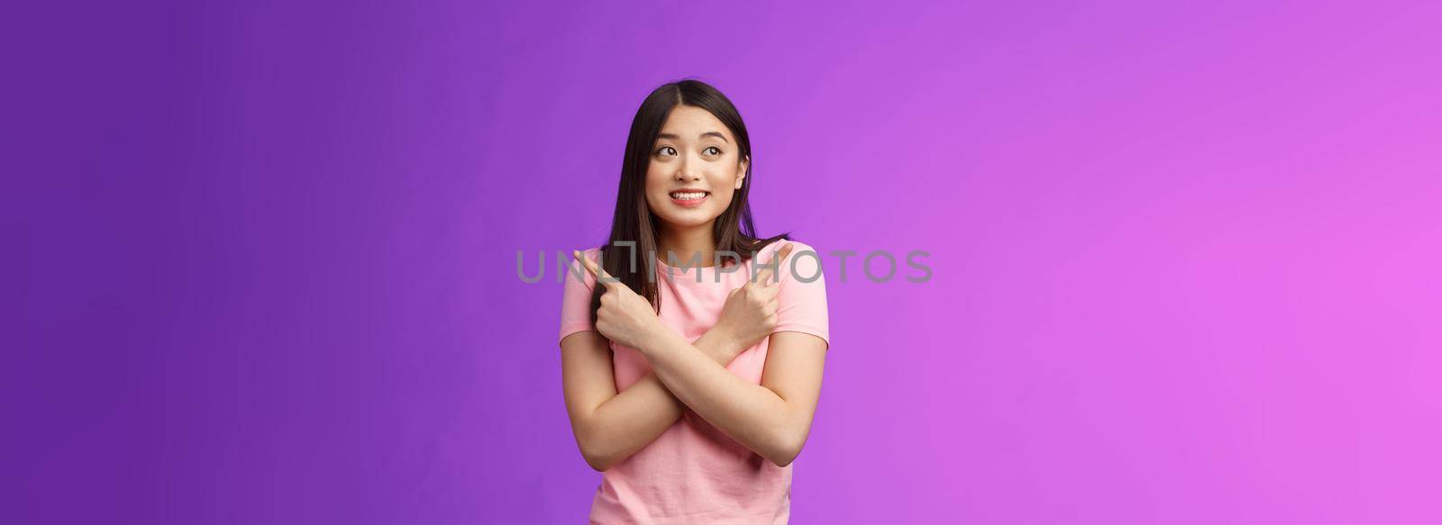 Cheerful timid cute asian girl, look tender, smiling gazing aside cross hands chest, pointing sideways, show left right, making decision, gathering confidence choose, purple background.