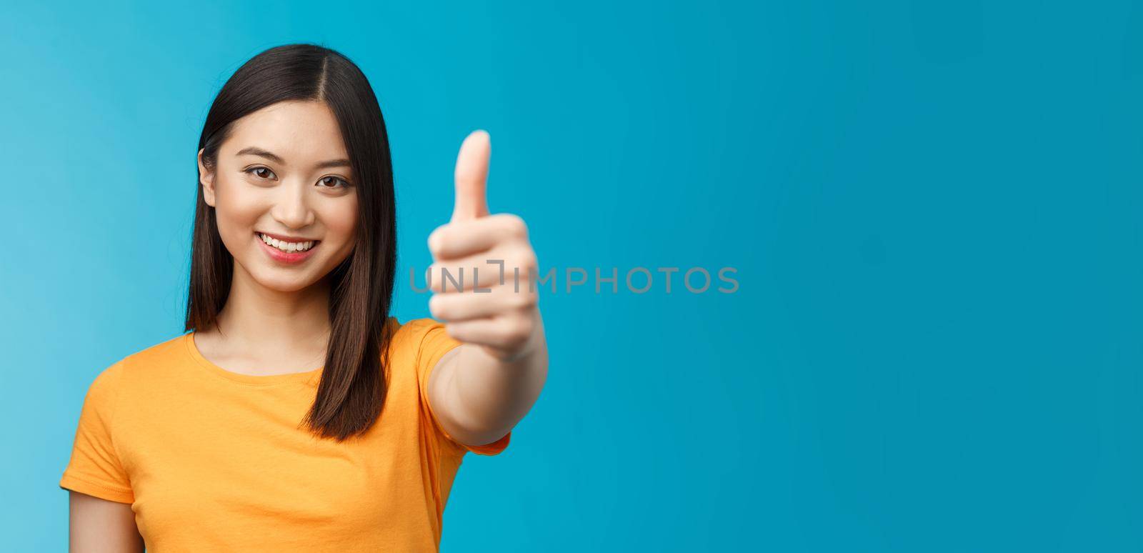 Close-up optimistic good-looking asian girl dark short haircut show thumb up, encourage friend congratulate good nice job, smiling delighted, give approval permission, stand blue background.