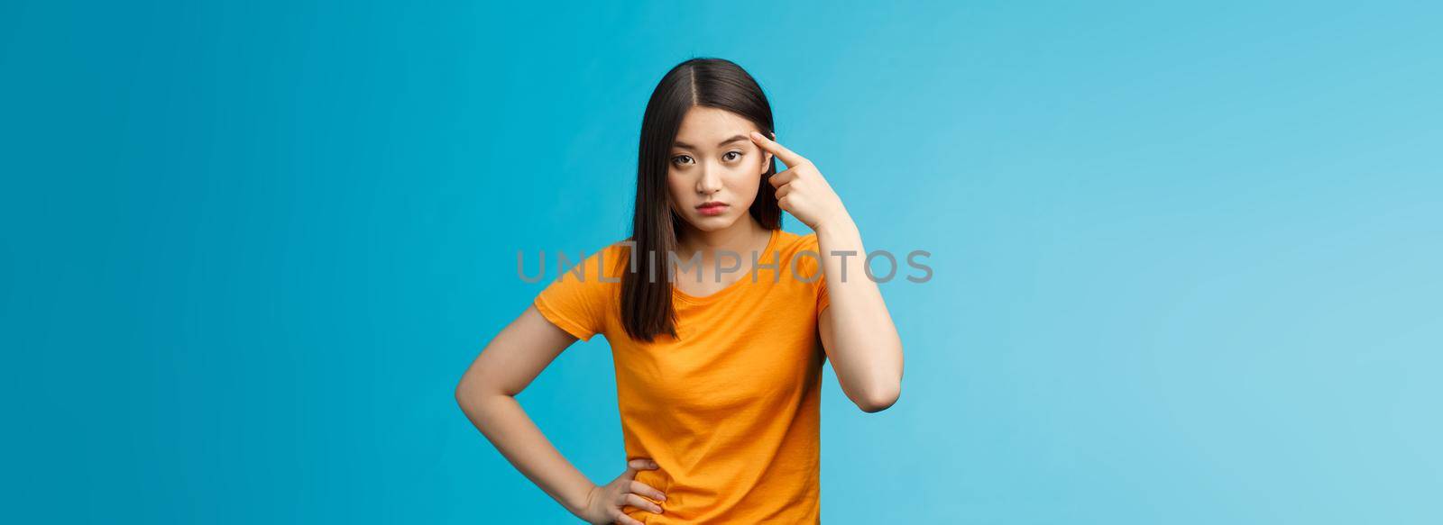 Pissed irritated asian girl look annoyed bend camera roll finger on temple stare camera bothered dismay, asking are you out mind, show person crazy weird, stand blue background. Copy space