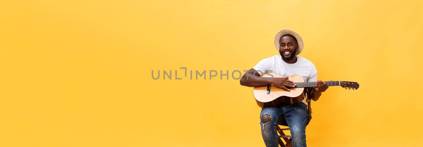 Handsome african american retro styled guitarist playing acoustic guitar isolated on yellow background