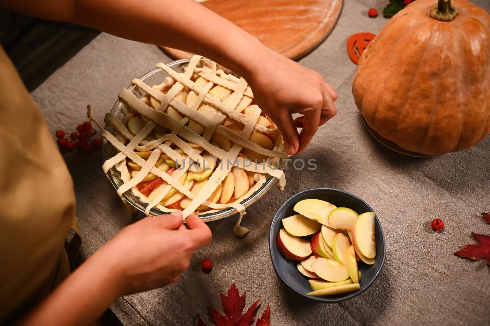 Top view housewife makes crusty lattice pattern from striped pastry dough, on top of pumpkin apple pie. Thanksgiving Day by artgf