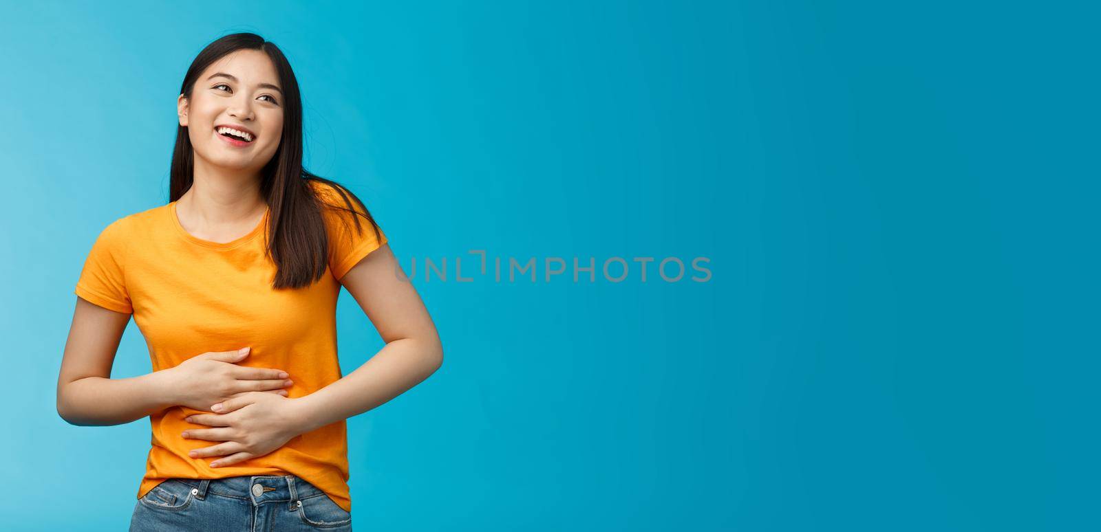 Happy staffed cute asian girl feelings satisfaction after eating favorite food, smiling broadly rubbing tummy, touch stomach from delight and joy, like eat delicious meals, stand blue background by Benzoix