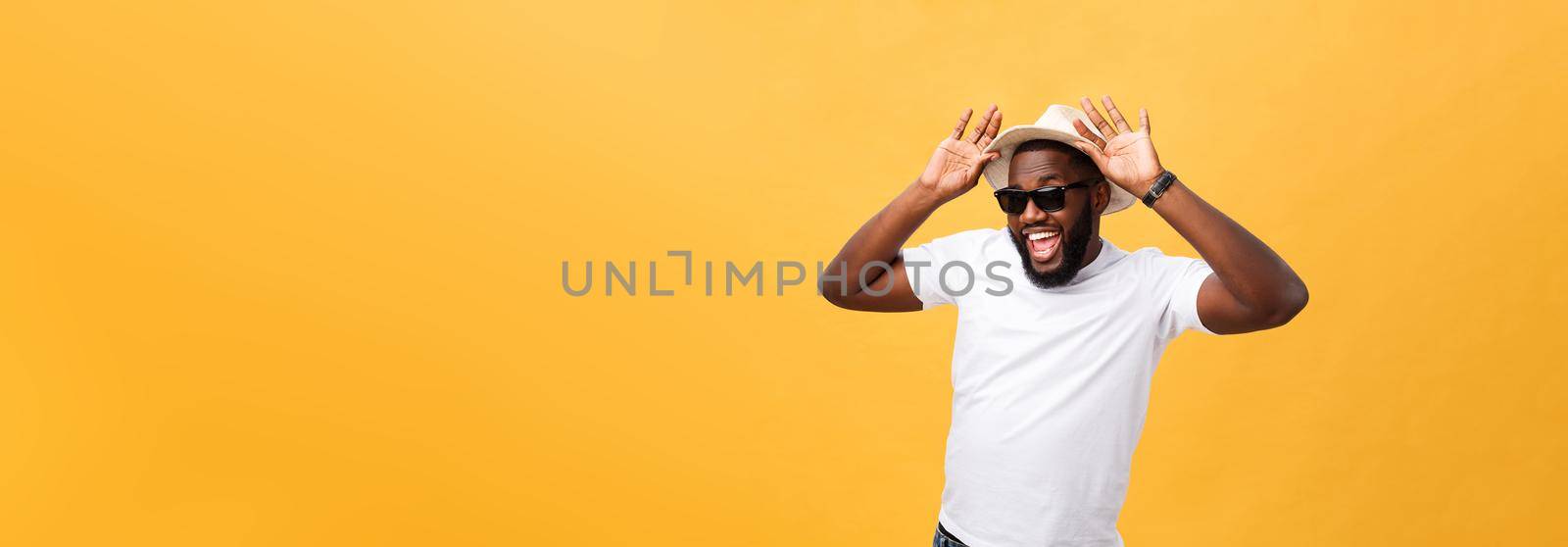 Close up portrait of a young man laughing with hands holding hat isolate over yellow background by Benzoix
