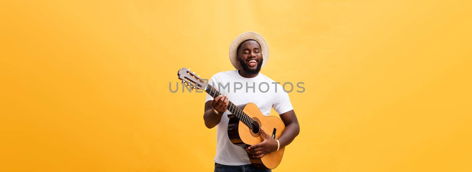 Handsome african american retro styled guitarist playing acoustic guitar isolated on yellow background
