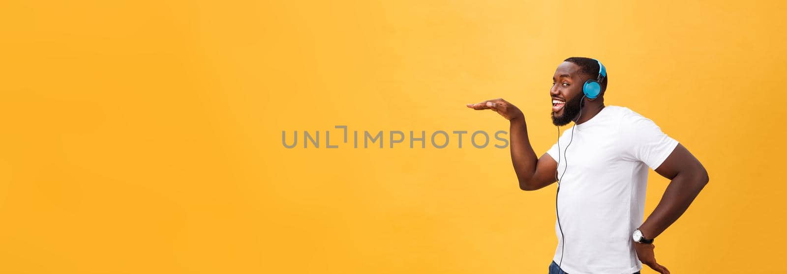 Young African American man wearing headphone and enjoy music dancing over yellow gold Background.