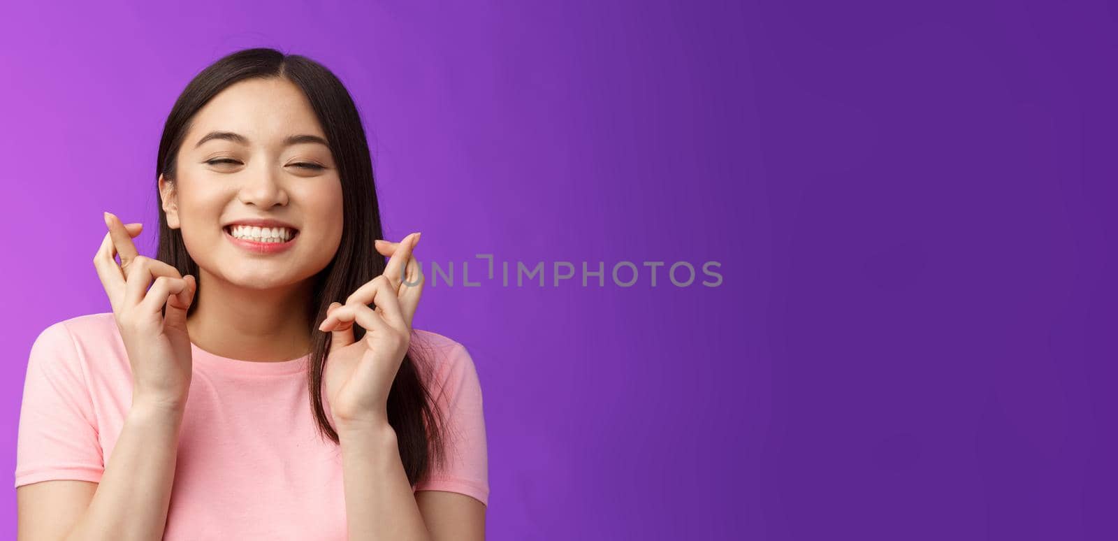 Headshot dreamy lucky cute asian girl believe she win, make wish, cross fingers good fortune, close eyes smiling happily feeling hopeful receive positive results, stand purple background.
