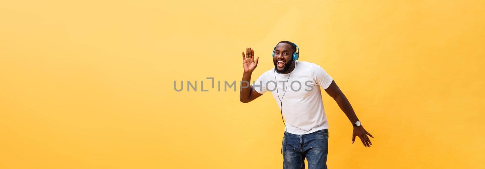 Full length portrait of a cherry young african american man listening to music with headphones and dancing isolated over yellow background by Benzoix