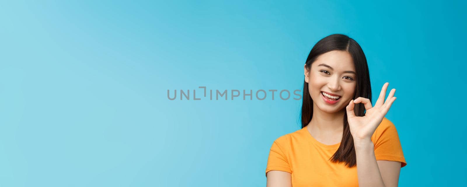 Close-up cute asian friendly girl supports your fantastic idea, smiling broadly, show okay ok sign approval, accept terms, agree take part event, stand blue background satisfied, judging nice work by Benzoix