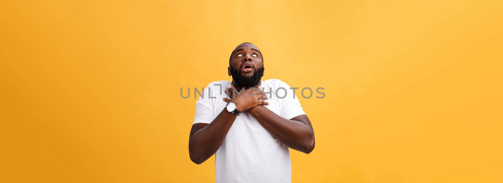 Portrait of african american man with hands raised in shock and disbelief. Isolated over yellow background