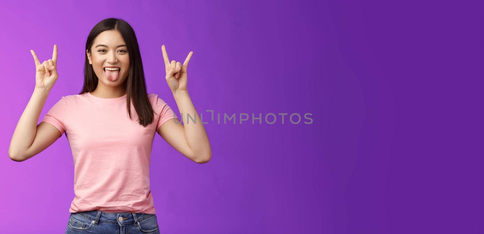 Rebellious amused asian girl enjoy rock-n-roll, attend awesome concert have fun, show tongue make heavy-metal gesture, express excitement and joy, stand purple background cheerful by Benzoix